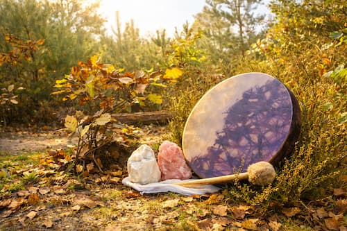 Tambour chamanique posé dans les bois par un matin d’automne, entouré de feuilles dorées et de cristaux éclairés par une lumière douce et dorée.