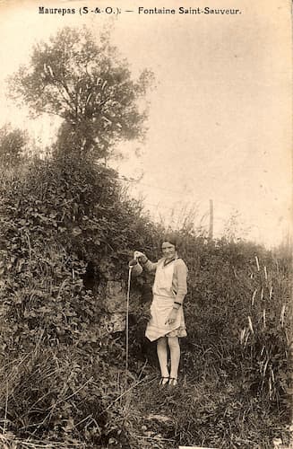 Ancienne carte postale montrant une jeune fille debout devant la fontaine St-Sauveur versant de l’eau.